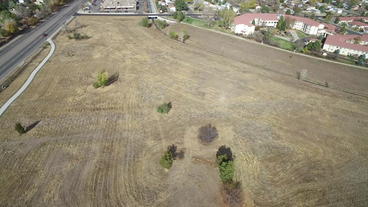 Aerial view of a field with a paved path, roadside, and homes at the edge.