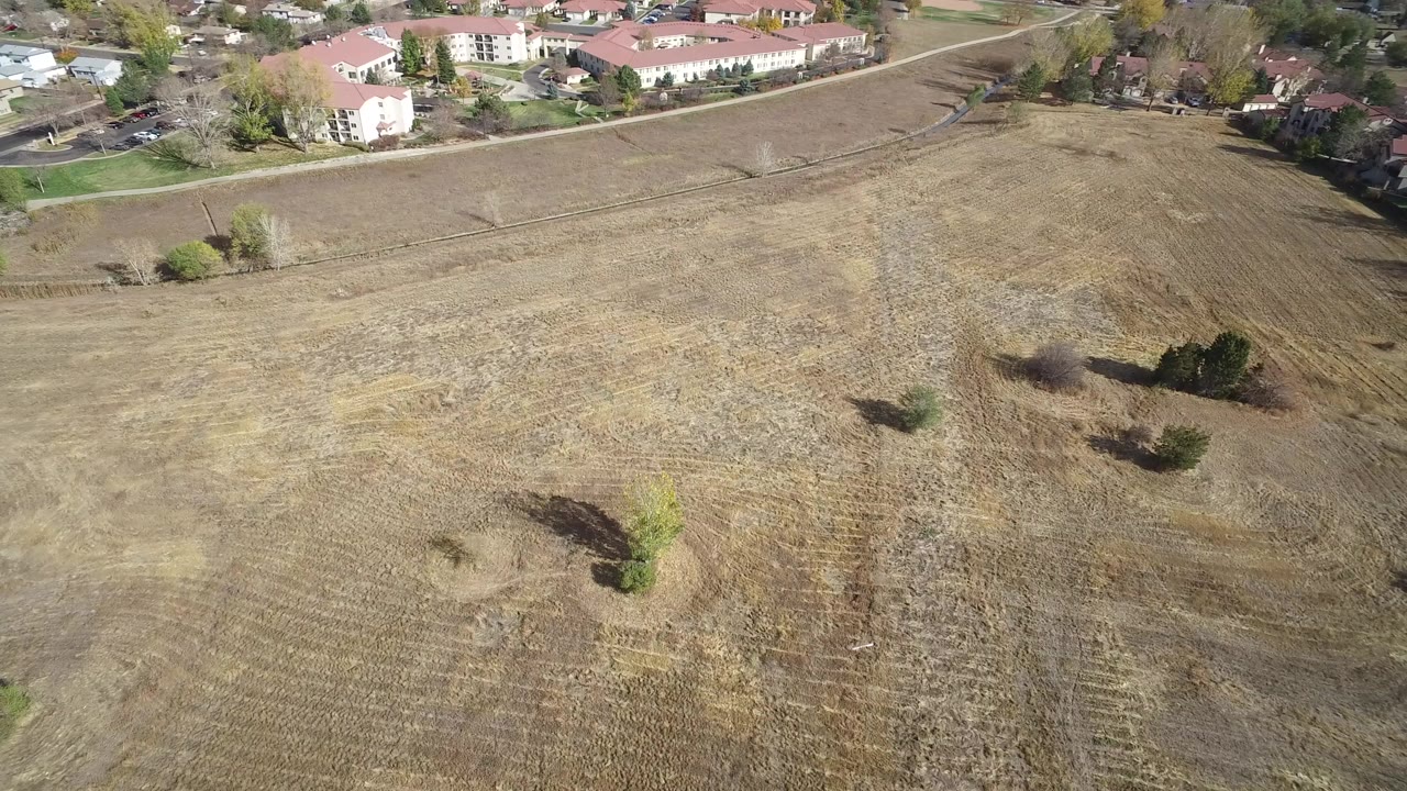 Aerial view of a dry vacant field beside residential buildings.