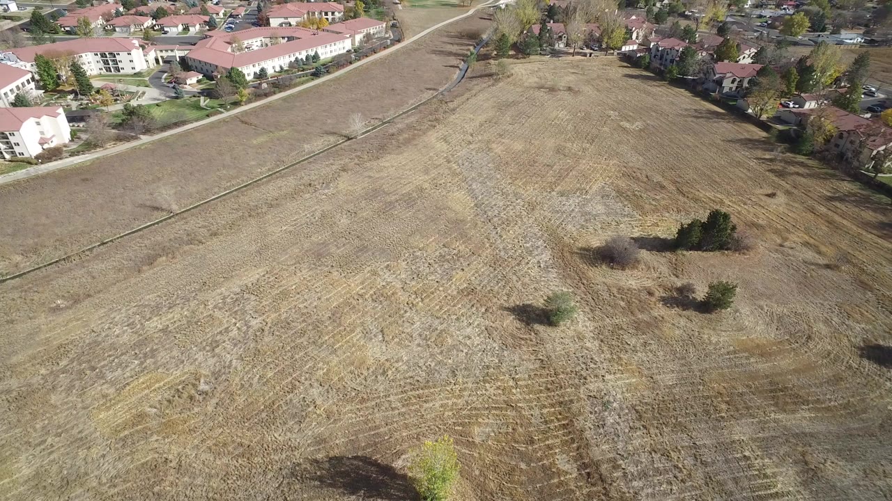 Aerial view of a dry open field beside red-roofed residential buildings.