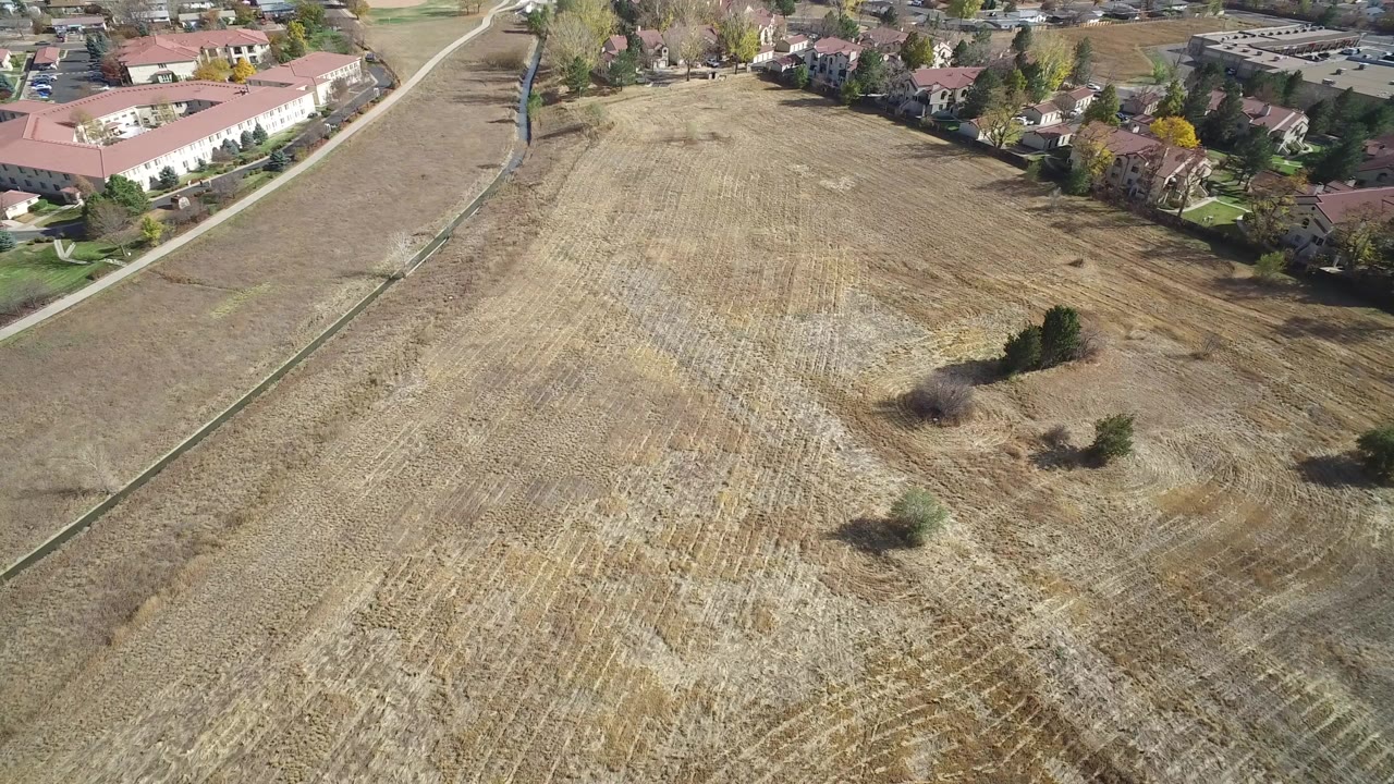 Aerial view of a brown field beside homes and an irrigation ditch.