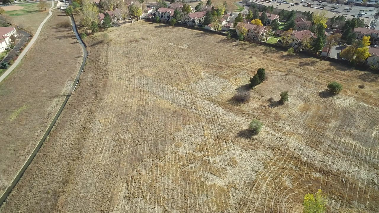 Aerial view in Hidden Lake, Colorado, looking across dry field stubble toward a line of residential homes, with a narrow path at left and no visible people.