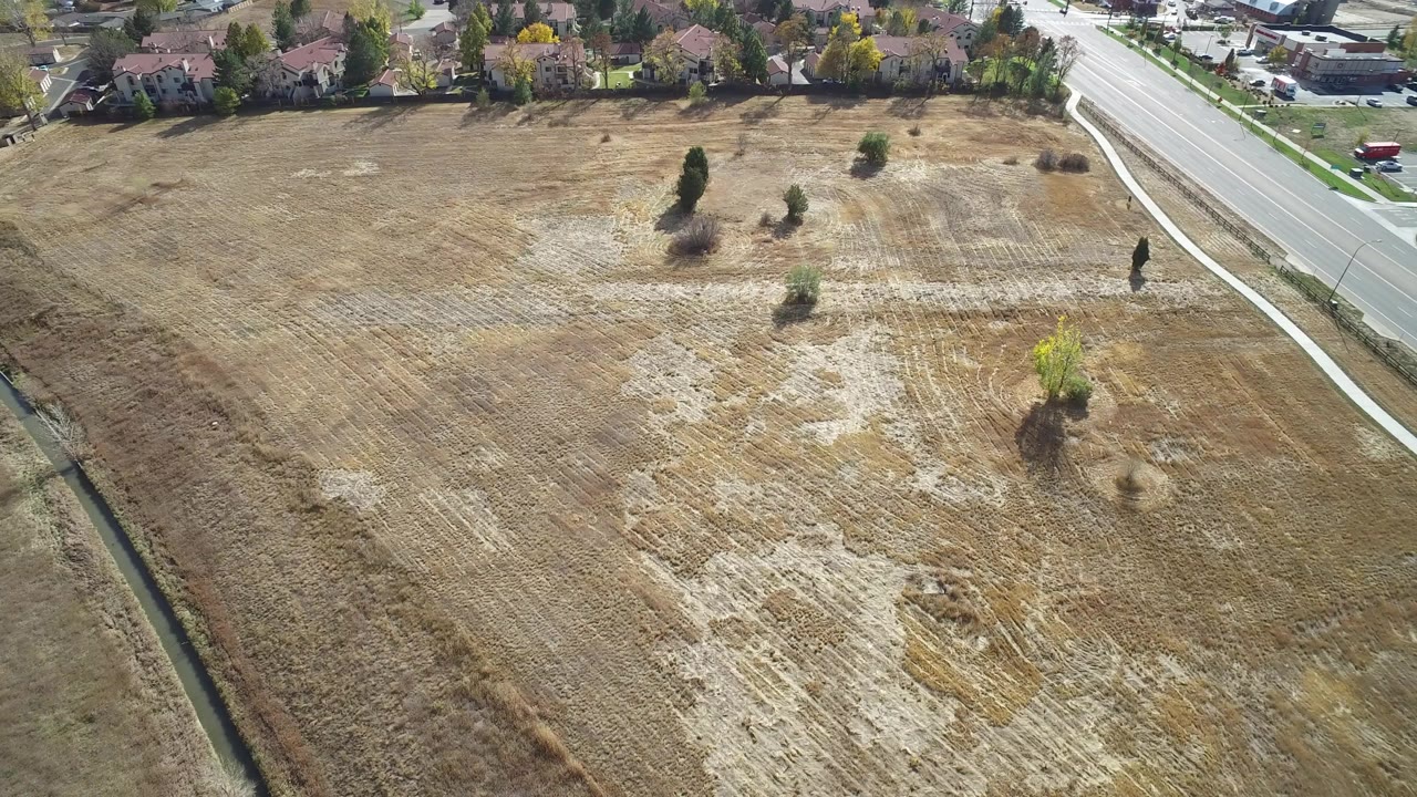Aerial view of a dry field beside a road and suburban homes.