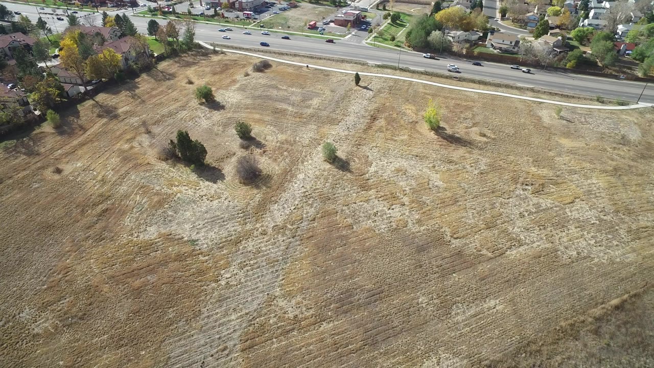 Aerial view of a dry field beside a busy road and houses.