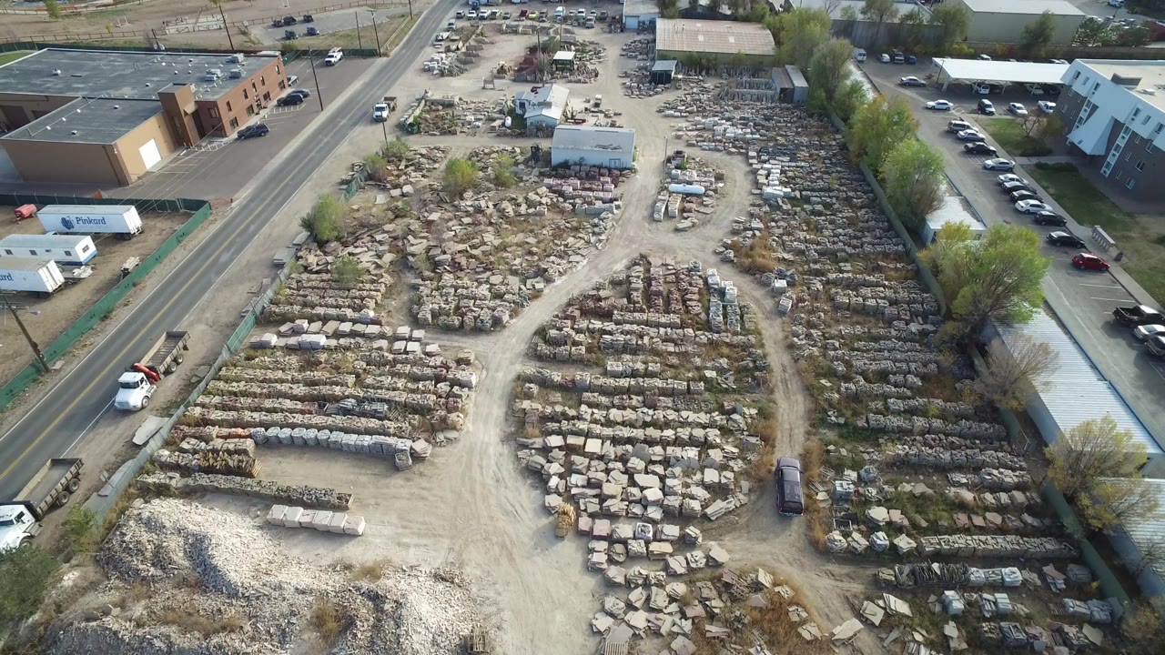 Aerial view of an outdoor materials yard beside roads and warehouse buildings.