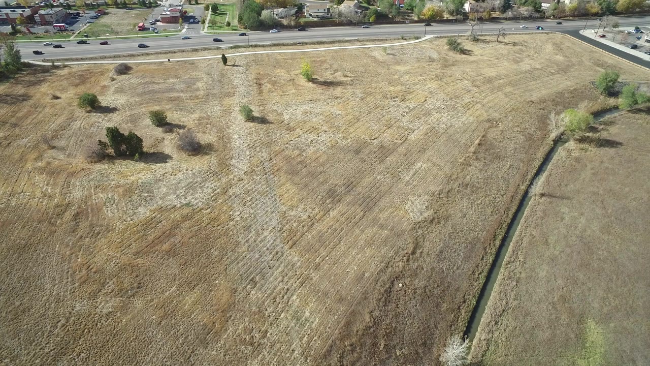 Aerial view over dry fields with shrubs and a road at the top of frame.