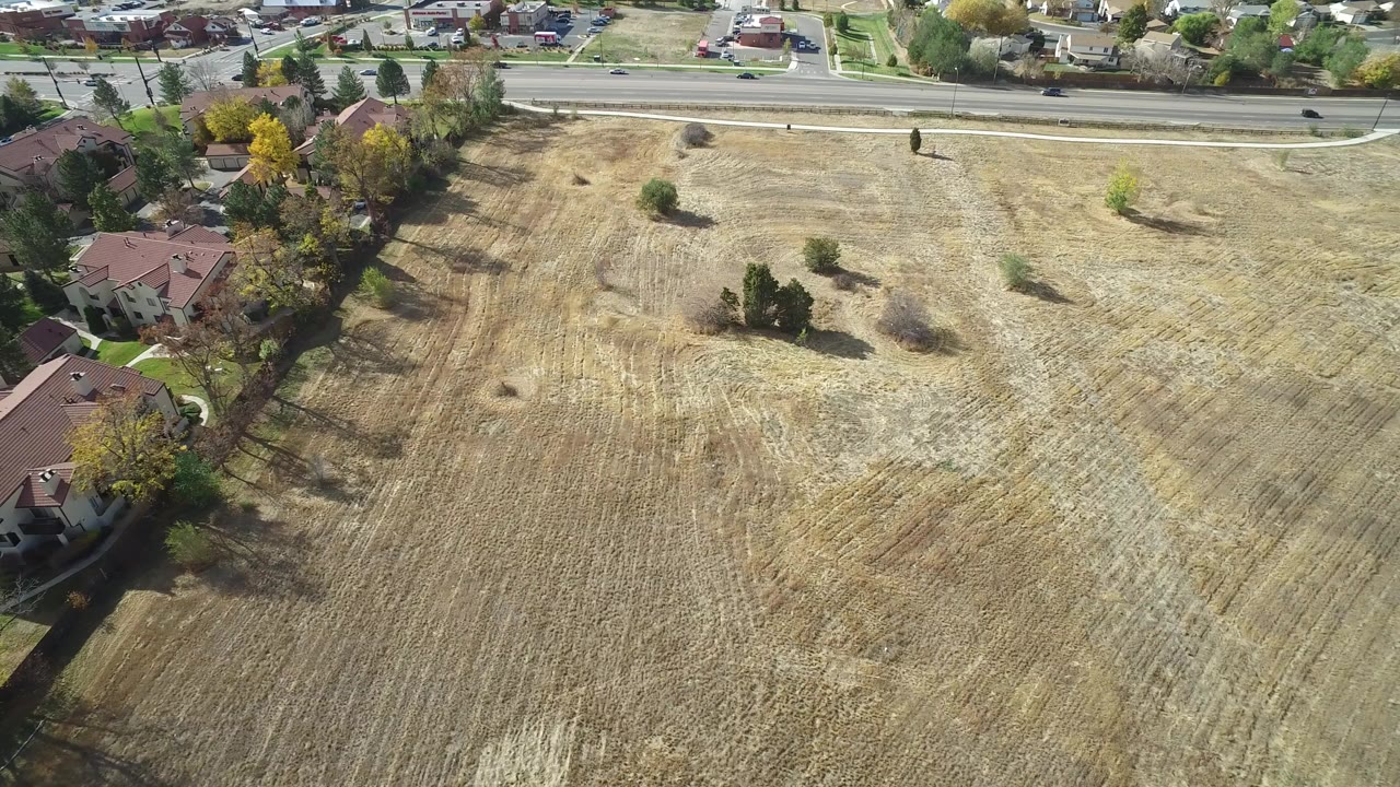Aerial view over a dry field beside suburban houses and a road.