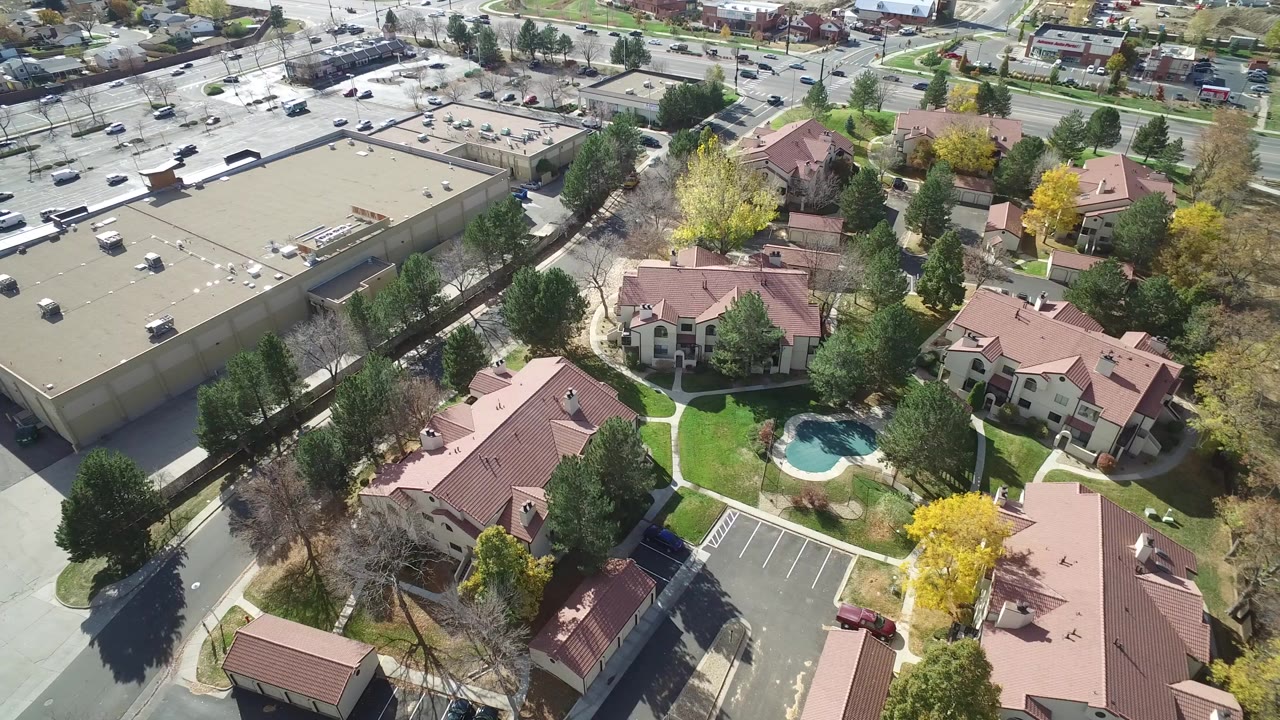 Aerial view of a mall parking lot beside red-roof residential buildings and trees.