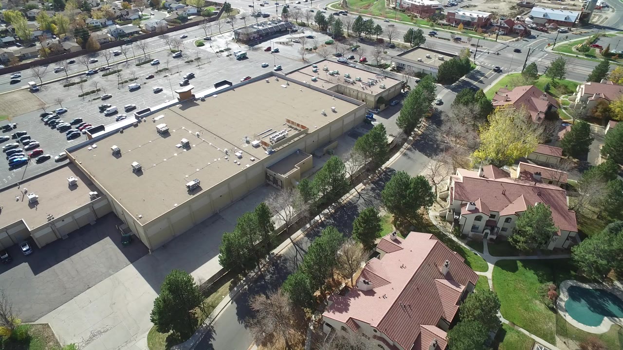 Aerial view of a flat-roofed commercial building beside parking lots and homes.