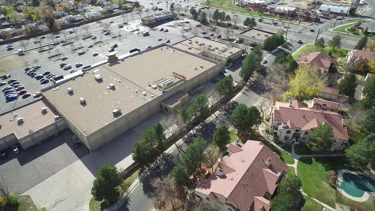 Second frame over Hidden Lake, Colorado, with the beige commercial roof centered, a parking lot to the upper left, residential buildings to the lower right, and no visible people.