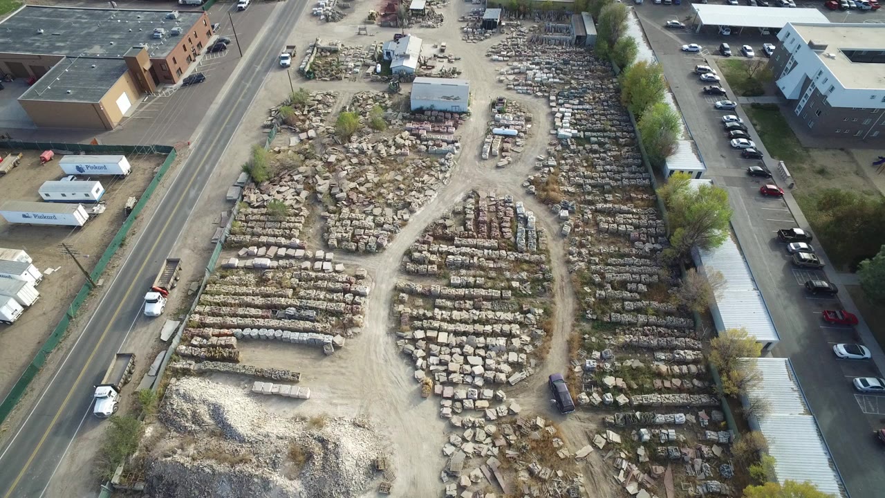 Opening aerial frame over Hidden Lake, Colorado, showing a dusty industrial storage yard beside roads and low buildings, with rows of small objects and no visible people.