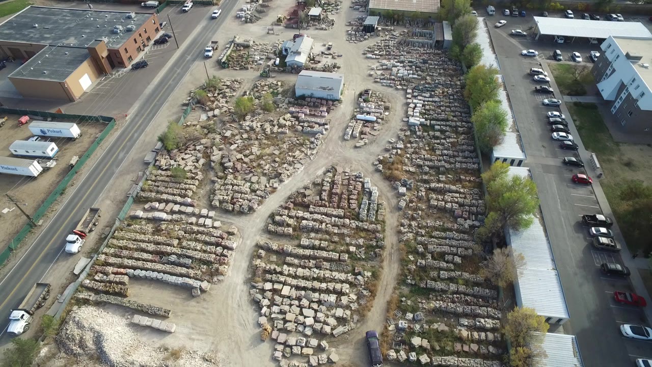 Aerial view of an outdoor warehouse yard filled with rows of stone blocks beside roads and low buildings.