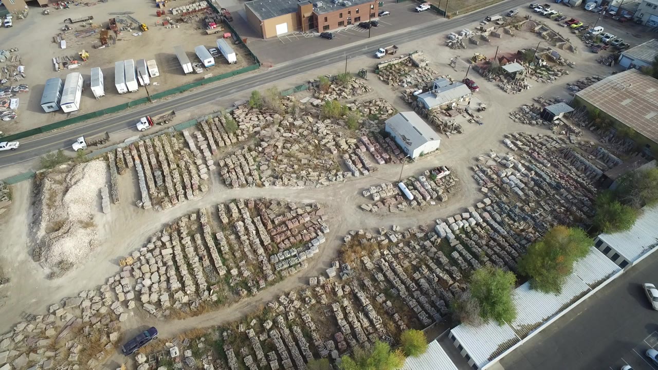 Aerial view of a material yard, roads, buildings, trees, and parked vehicles.