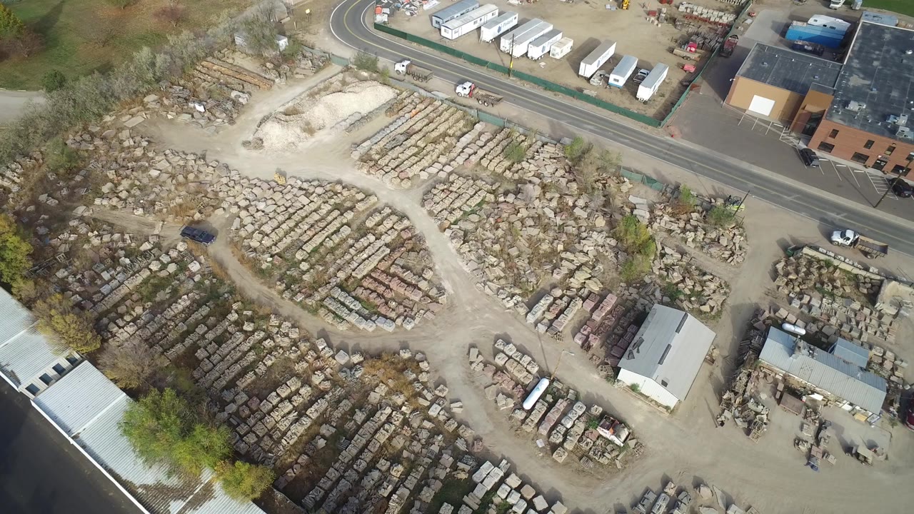 Overhead view of a scrap yard beside a paved road and industrial buildings.