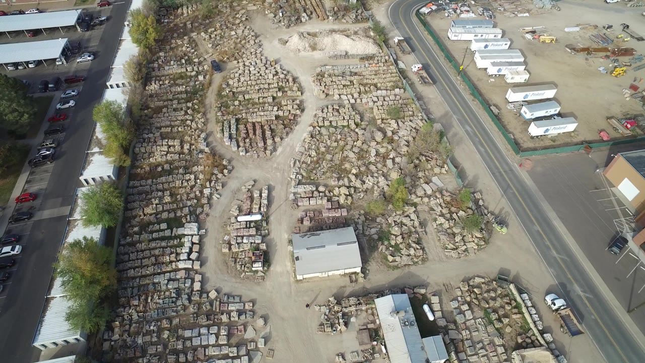 Overhead view of a gravel yard, road, parked cars, and low buildings.