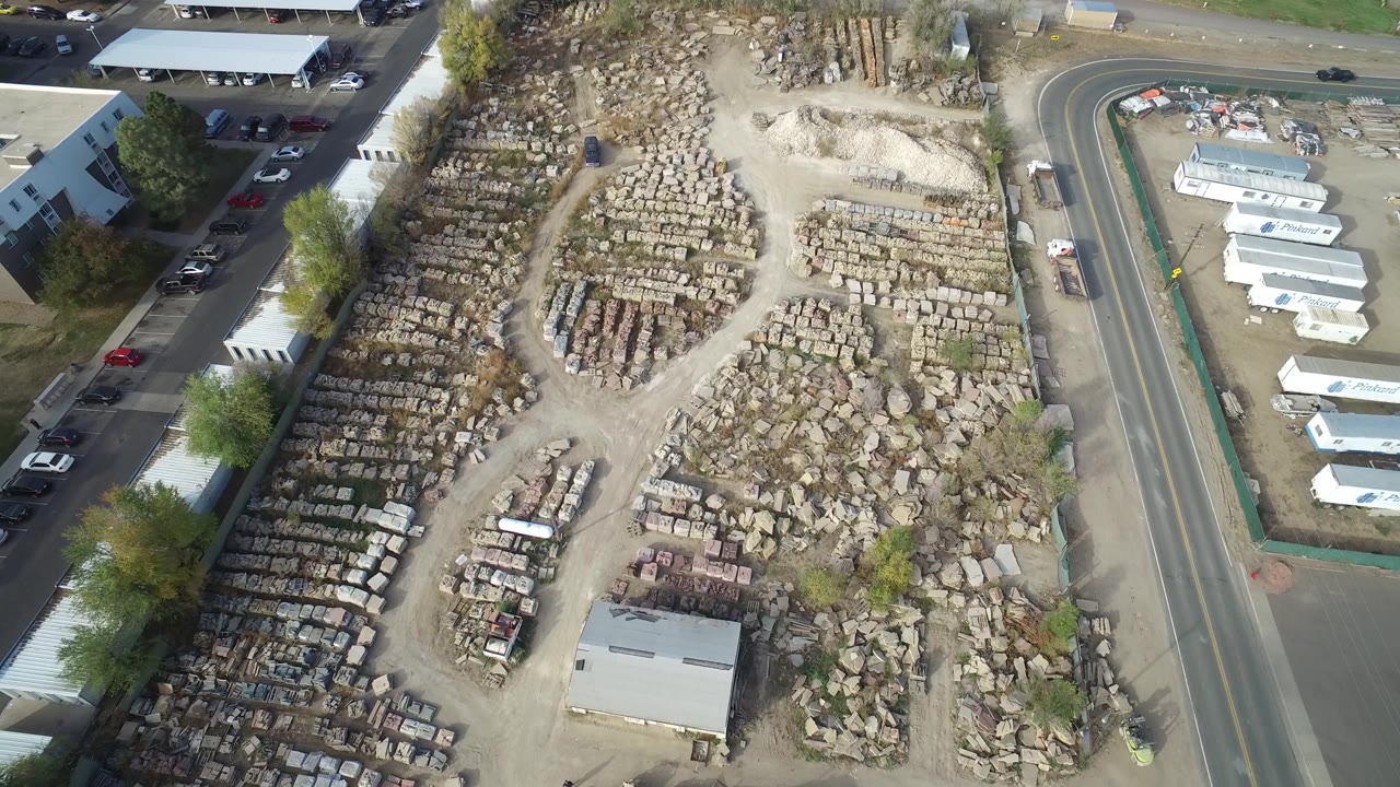 Drone-like view of stone piles, debris, a shed, and roadside trailers.
