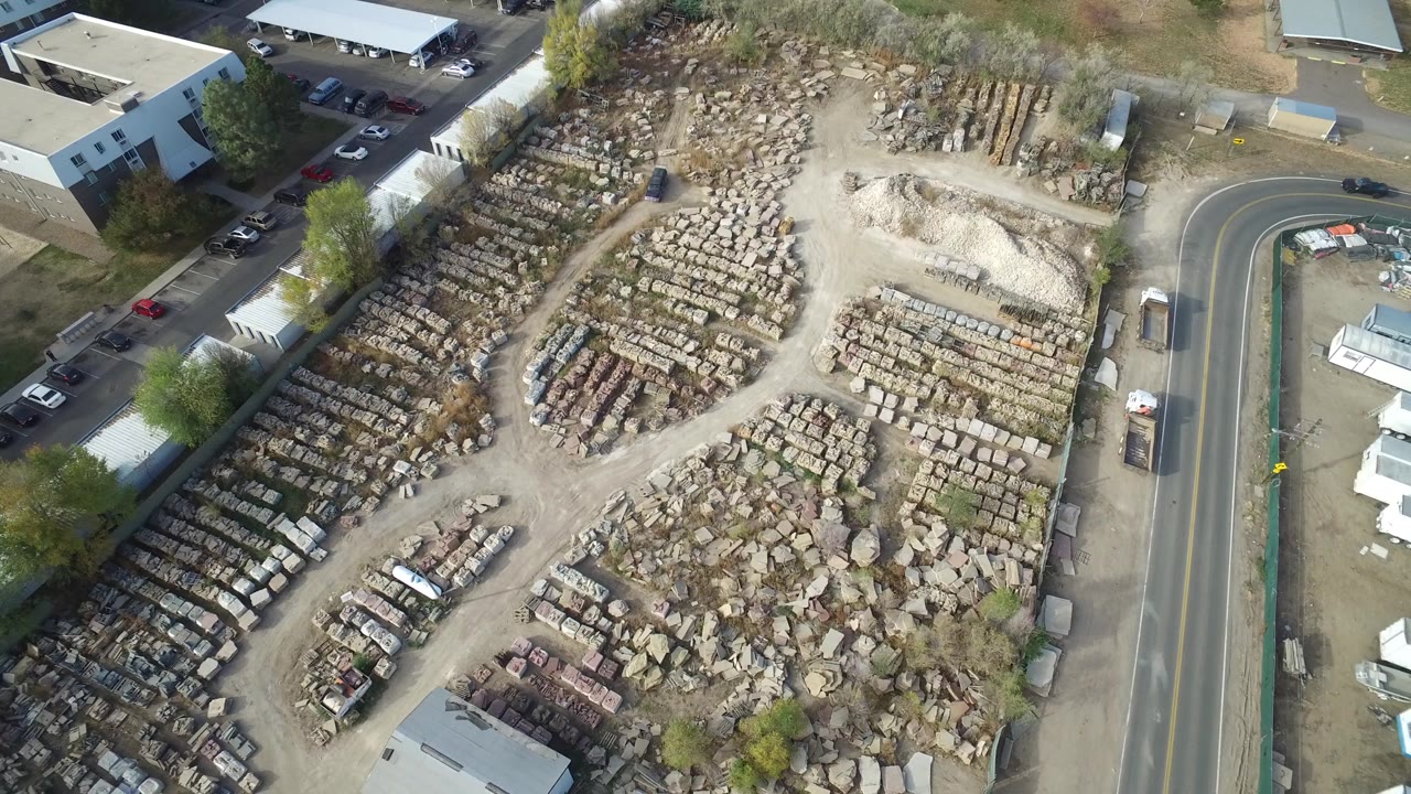 Aerial view of a large material lot beside a curved road and buildings.