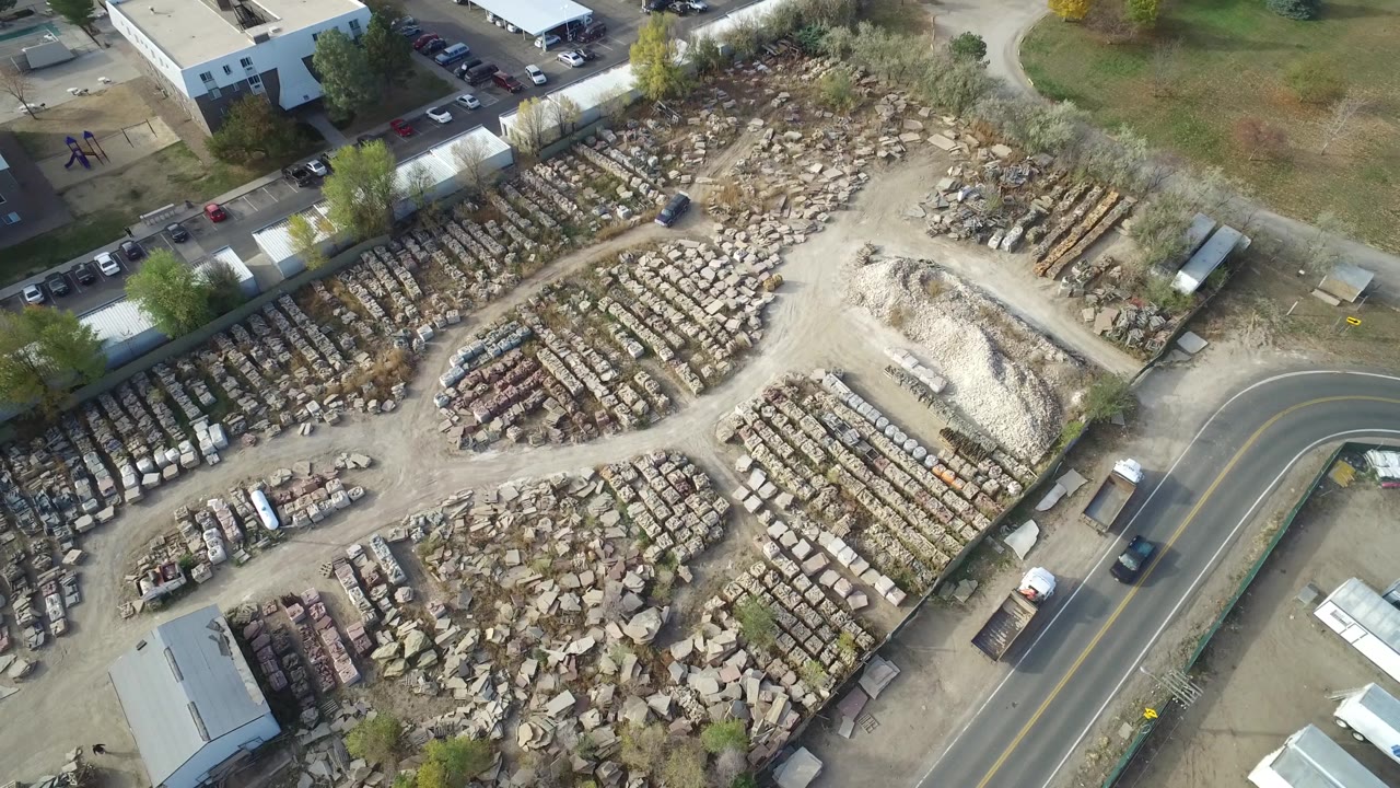 Drone view of a large yard filled with stone rows near buildings and roads.