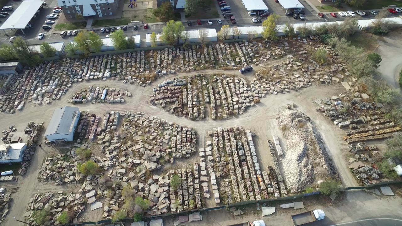Hidden Lake, Colorado aerial frame with dense rows of stone slabs or pallets, a pale dirt road through the yard, utility buildings, parked vehicles, and no visible people.