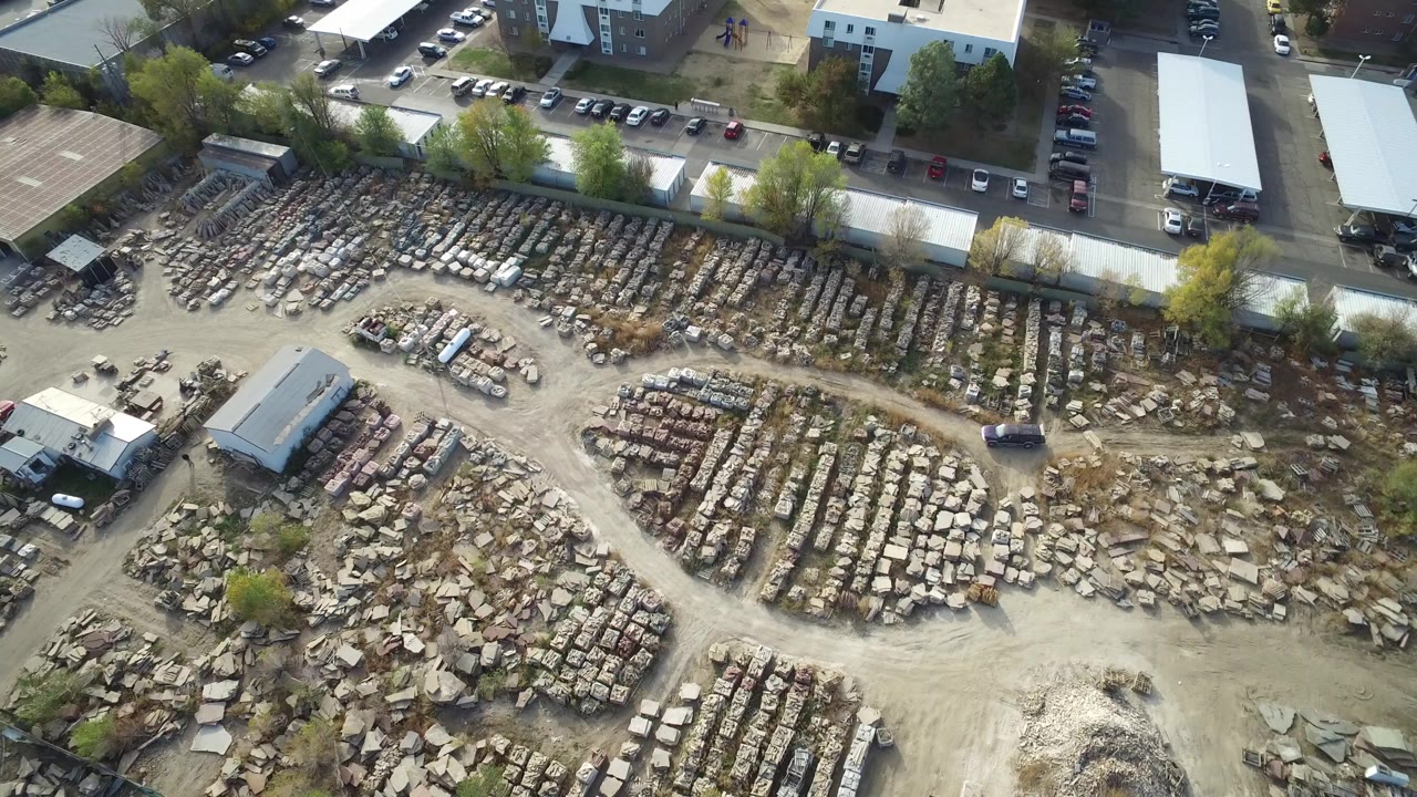 Aerial view of stacked stone rows, dirt lanes, buildings, and parked cars.