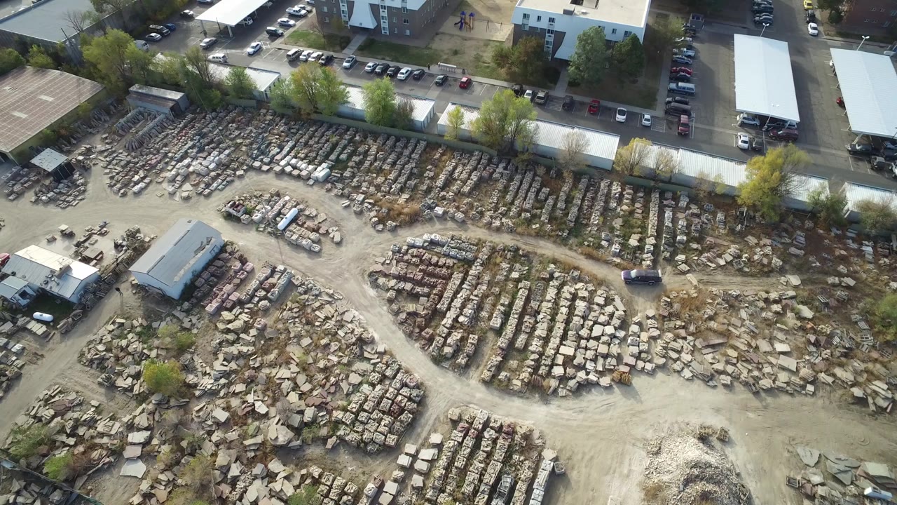 Aerial frame in Hidden Lake, Colorado showing the stone storage yard centered below a line of parked cars and flat-roofed buildings, with no visible people.