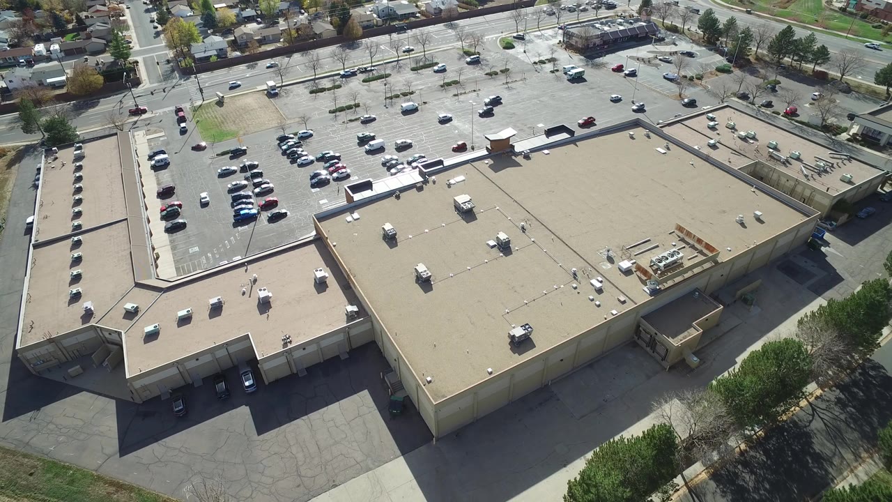 Drone-like view of a mall-like building with cars in adjacent lots.
