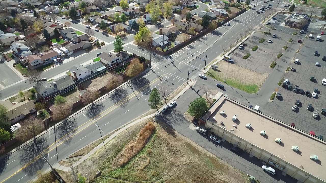 Early frame from Hidden Lake, Colorado showing an overhead view of a multi-lane road, adjacent homes, a parking lot, dry grass, and no visible people.
