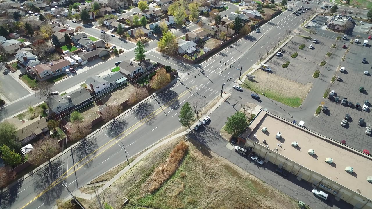 Drone-style overhead view of a suburban block beside a large road and parking lot.