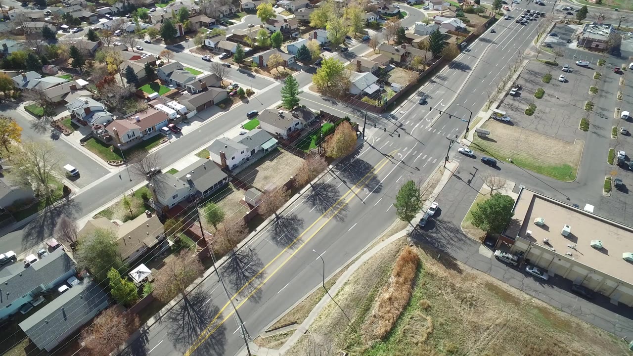 Aerial view of a suburban road, houses, parking lot, and dry grassy parcel.