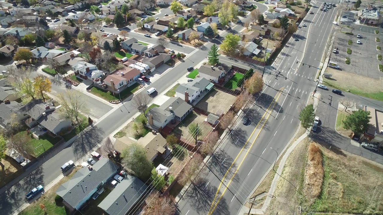 Aerial view in Hidden Lake, Colorado showing detached houses, intersecting residential streets, tree shadows, and light traffic on the main road with no visible people.