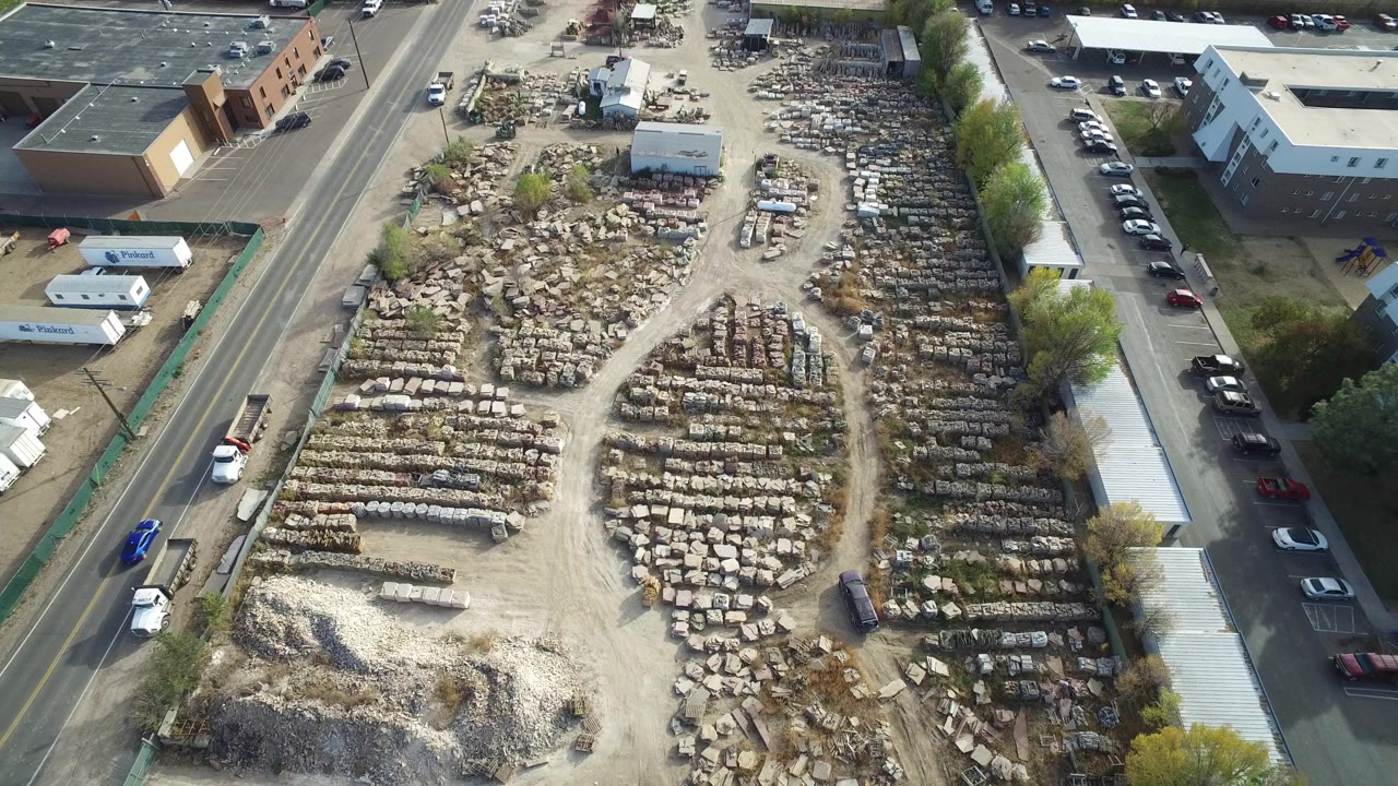Aerial view of a large materials yard beside roads and low buildings.