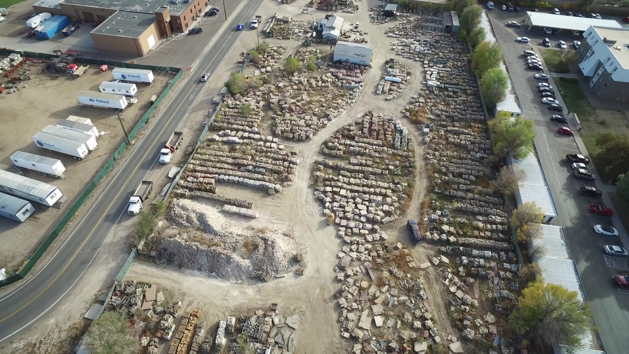 Aerial view of a dusty stone yard beside a road and low buildings.
