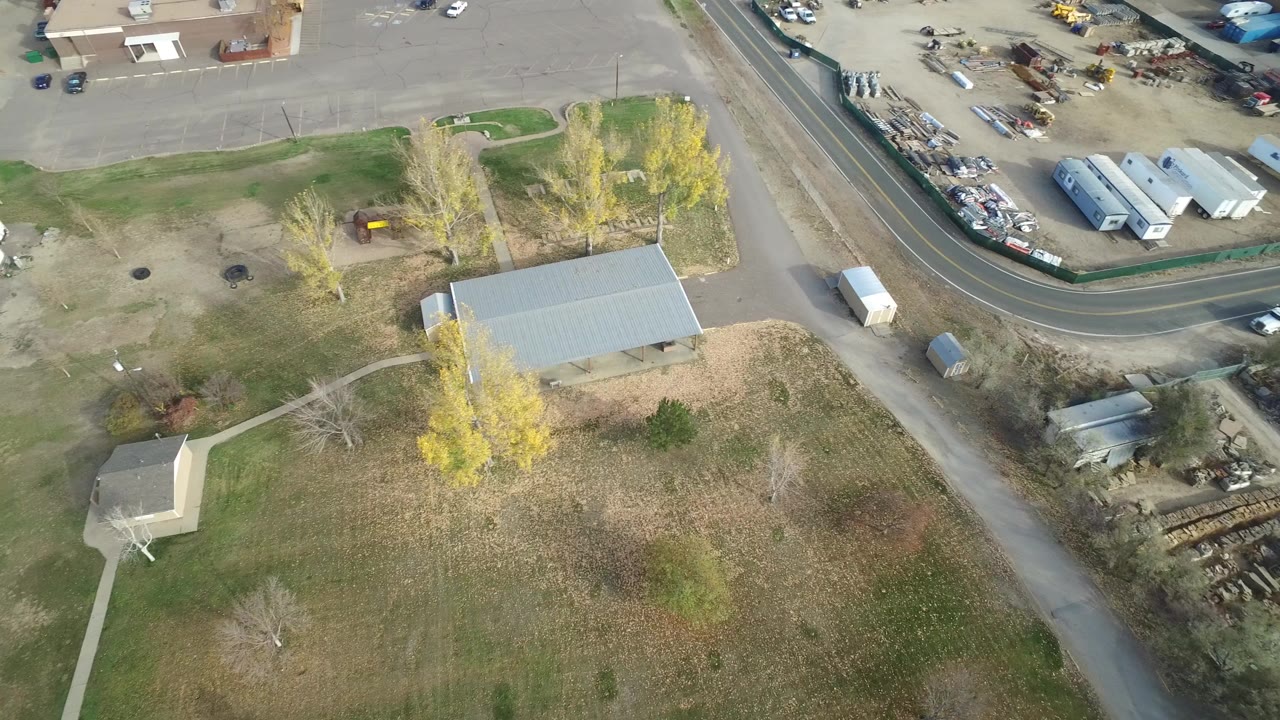 Overhead view of grass, roads, small buildings, and parked vehicles.