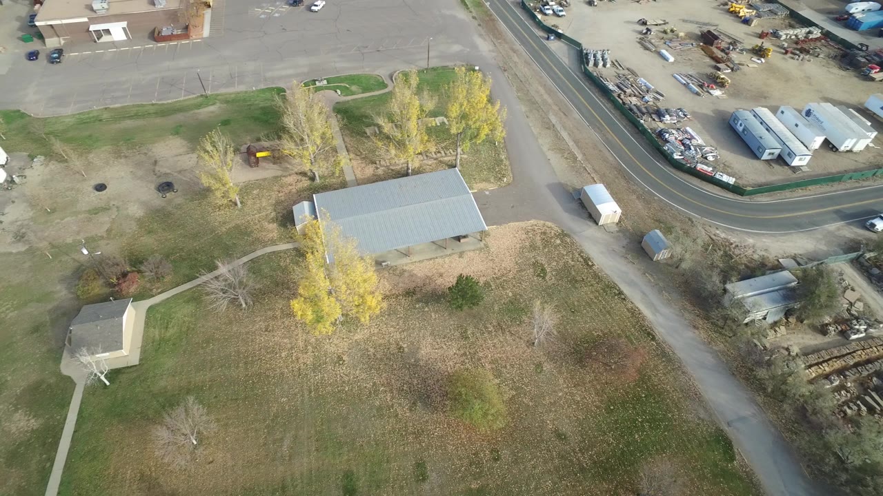 Drone view over Hidden Lake, Colorado showing a curved road, open grass, yellow trees, small sheds, parked RVs, and no visible people.