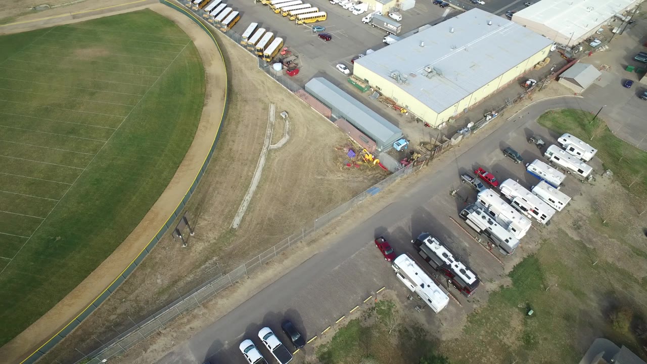 Aerial view in Hidden Lake, Colorado with more of the field grid visible, the service road running diagonally, and rows of vehicles and trailers near a large building.