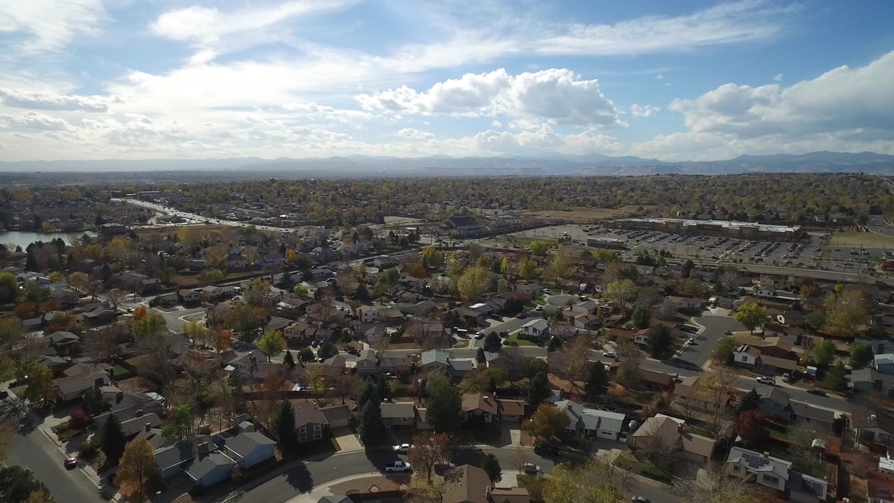 Aerial view over Hidden Lake, Colorado, with clustered homes in the foreground, a parking area and water in the midground, mountain ridges on the horizon, and no visible people.