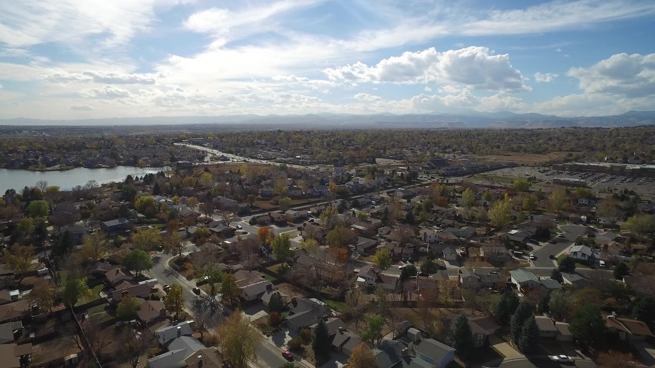 Aerial frame over Hidden Lake, Colorado with the lake shifted toward the left midground, rooftops and roads below, distant mountains, and no visible people.