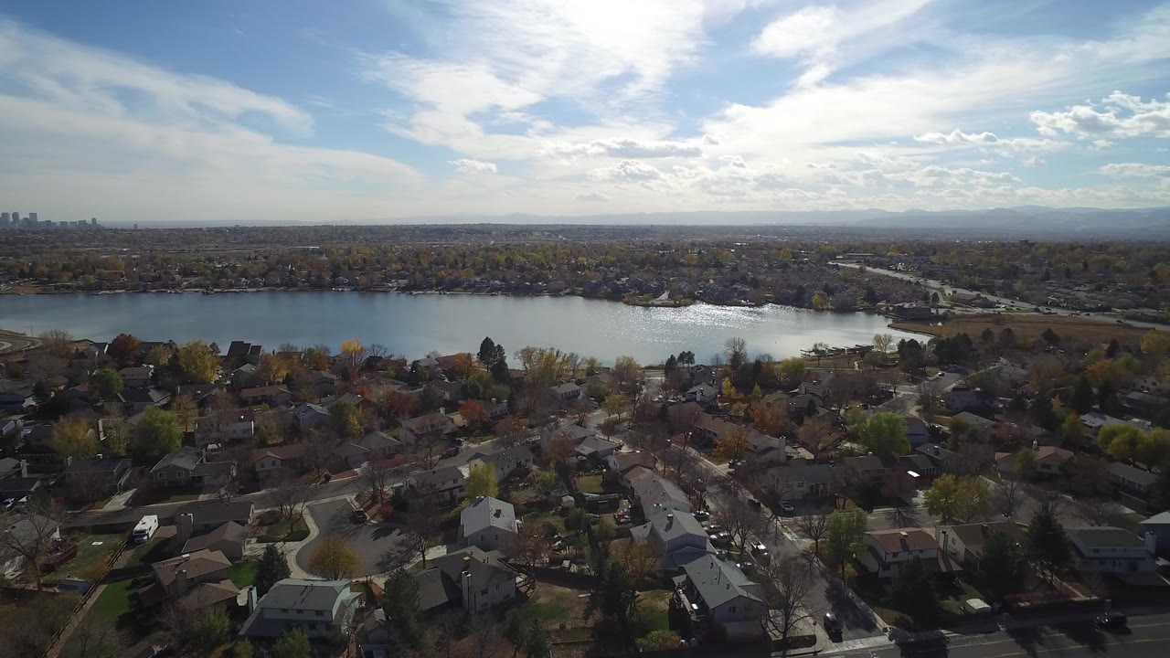 Wide aerial view of suburban homes beside a large lake under a bright sky.