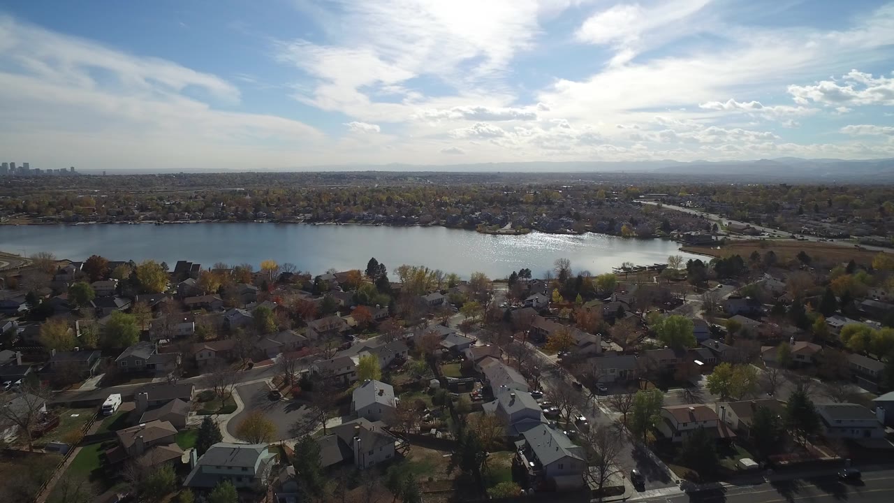 Hidden Lake, Colorado aerial frame with darker foreground rooftops, the lake stretching across the center, a hazy skyline at left, and no visible people.