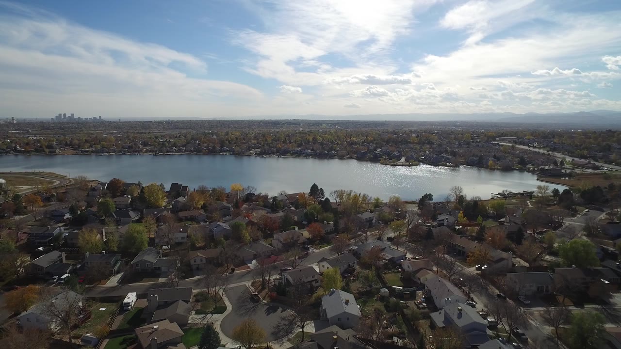 Aerial view of houses, trees, lake, distant skyline, and bright sky.