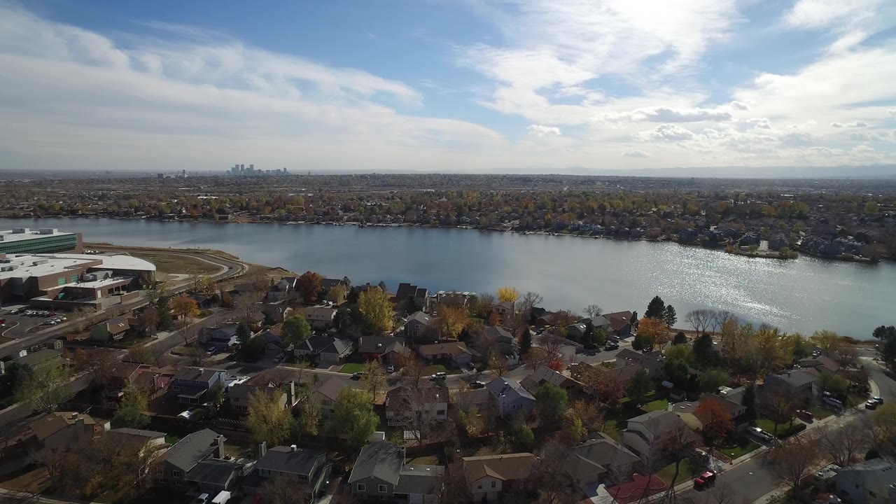 Aerial shoreline view with homes, lake, large building, and bright clouds