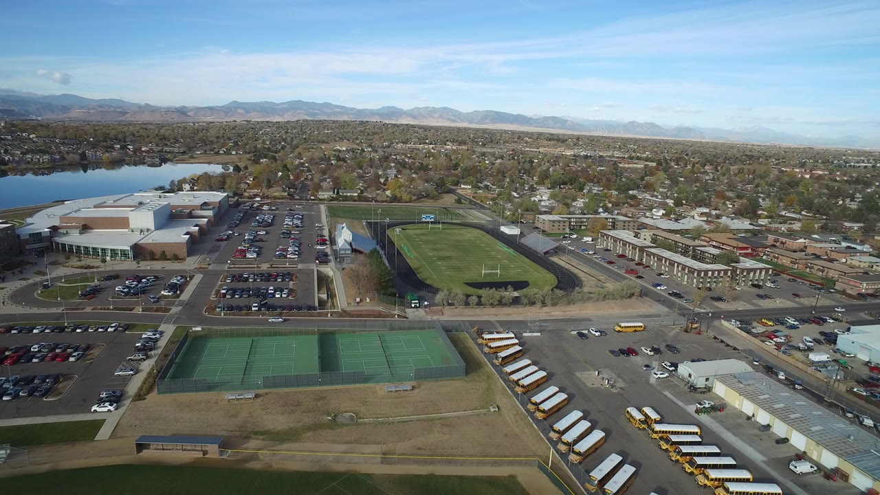 Aerial view of tennis courts, school buses, sports field, lake, and suburban streets.