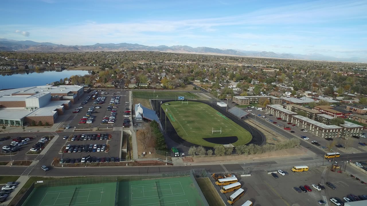 Aerial view of sports fields, parking lots, streets, homes, lake, and mountains.
