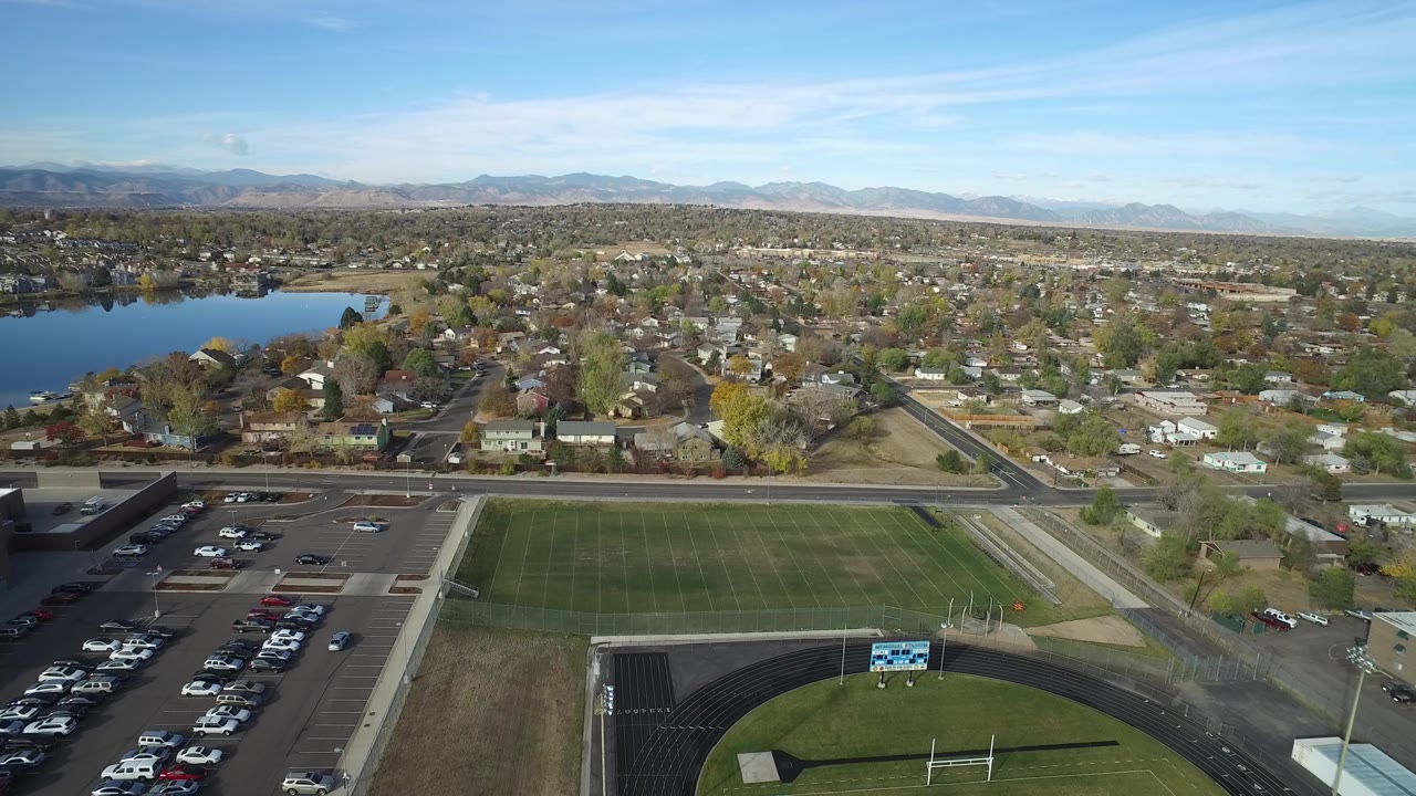 Drone-height suburban view with a lake at left, field below, and mountains on the horizon.
