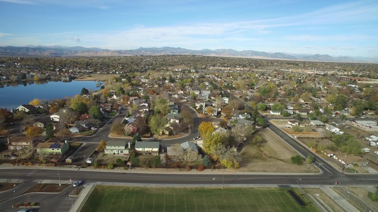 Drone-style view of homes, roadside, lake, and mountain backdrop.