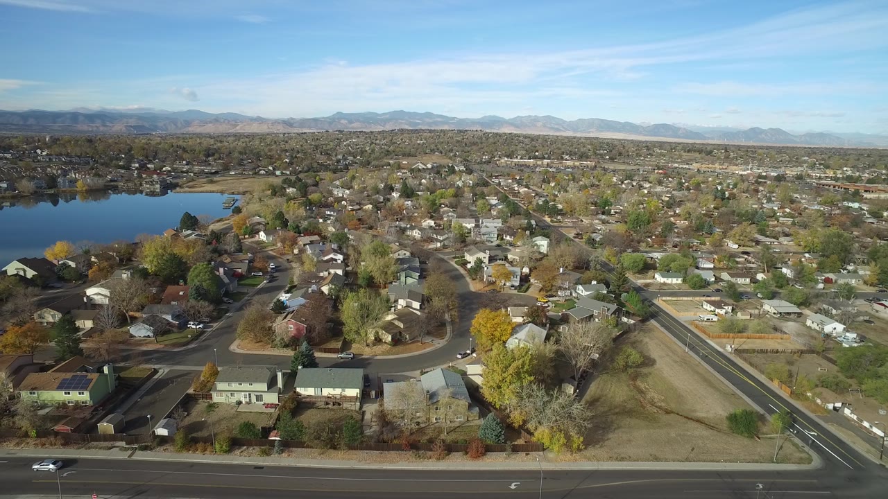 Drone-style aerial frame of Hidden Lake, Colorado, with the lake at left, clustered homes below, a straight road at right, and no visible people.