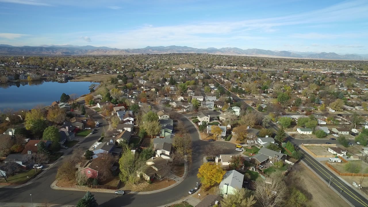 Aerial view of a lakeside neighborhood with curving streets and distant mountains.