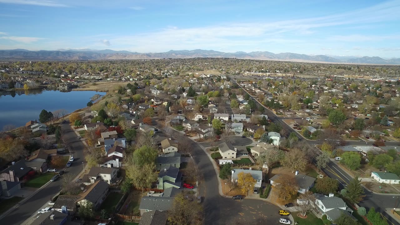 Wide aerial neighborhood view with lake and mountains.