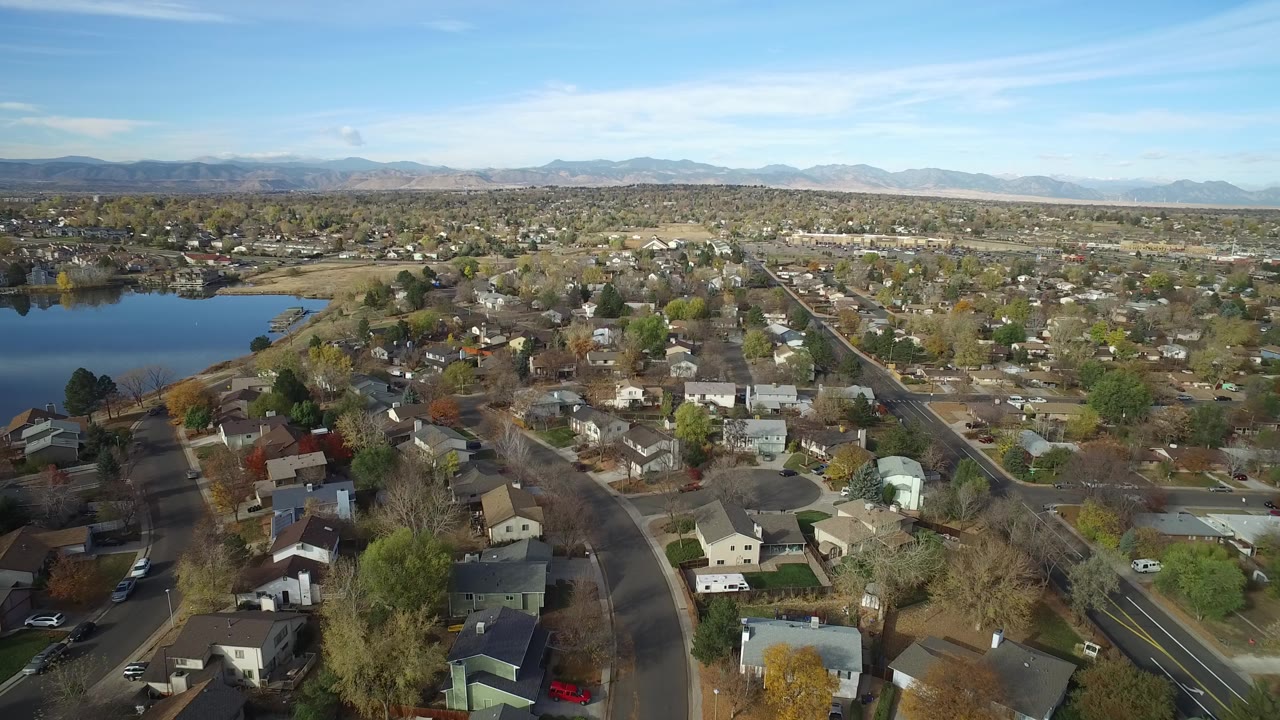 Aerial view of houses, roads, trees, lake water, and distant mountains.