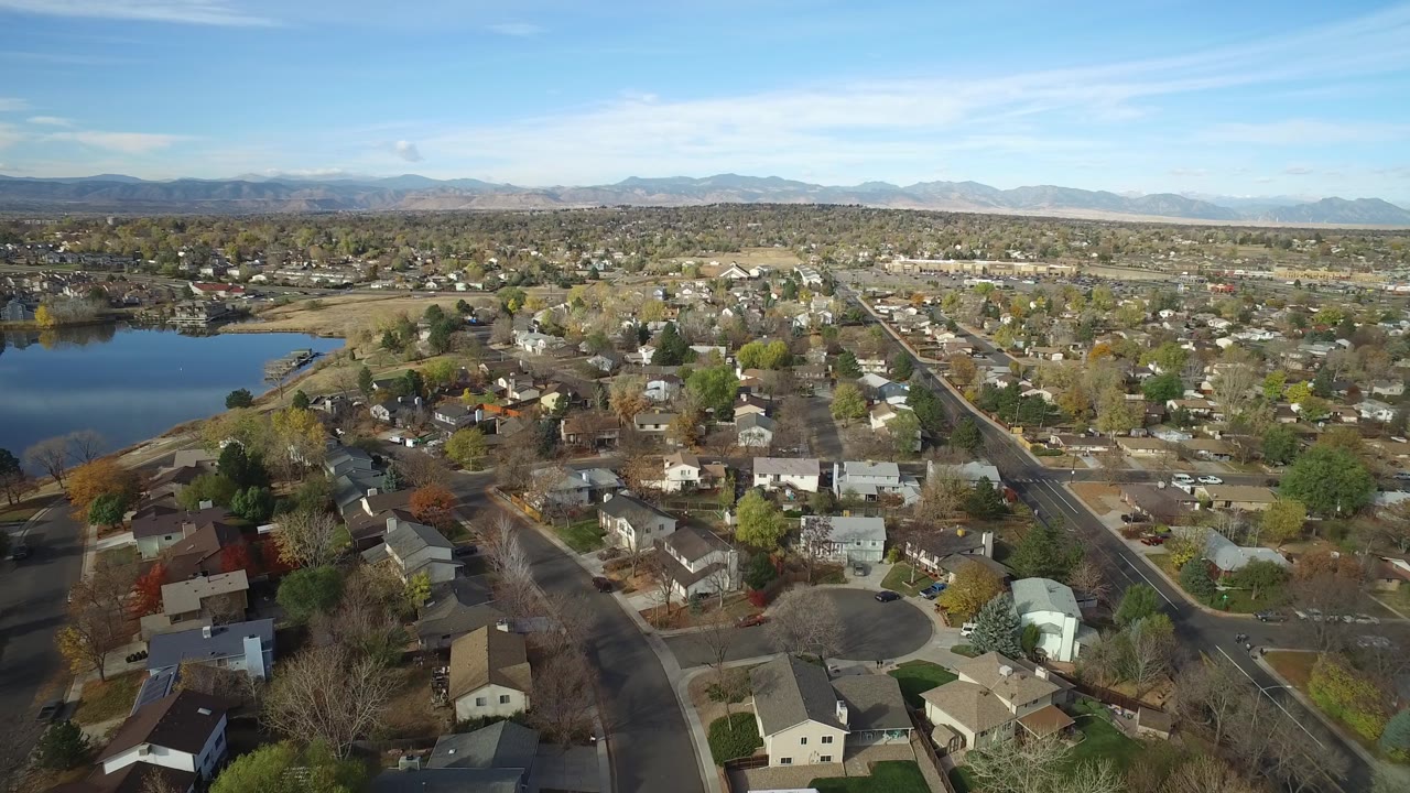 Wide aerial neighborhood view with lake water and mountain horizon.