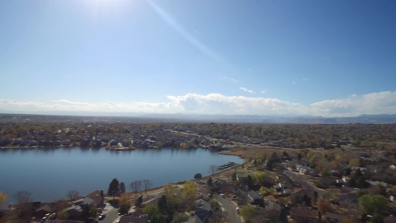 Aerial view of a lake, shoreline homes, roads, trees, and mountains in the distance.
